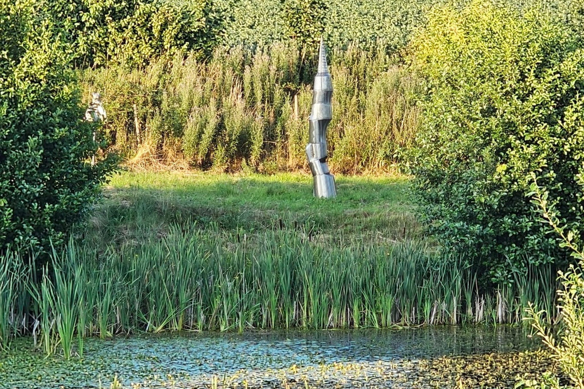 Metallskulptur im Skulpturenpark, gesehen über einen Teich und mehrere Landschaftsebenen
